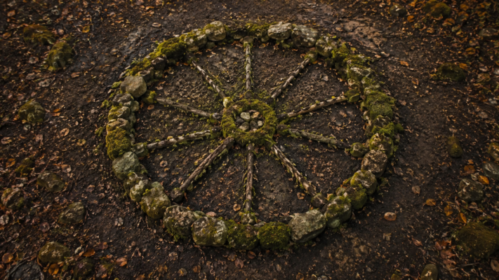 The Celtic Wheel of the Year represented in moss, stone, and branches on dark earth, viewed from above in soft autumn light.
